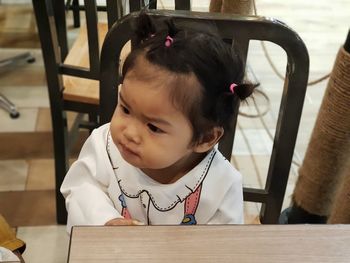 High angle view of cute baby girl looking away while sitting on chair