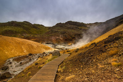 Boardwalk leading towards hot spring against sky