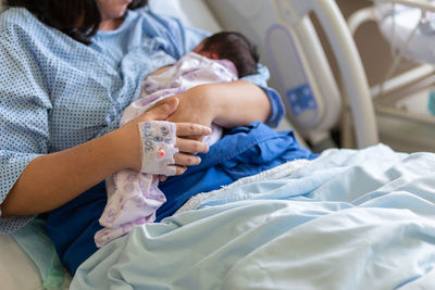 Midsection of woman breastfeeding baby in hospital