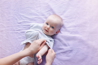 Cropped hands of mother holding cute daughter lying on bed at home