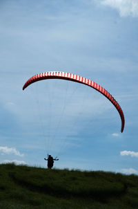 Person paragliding over field against sky