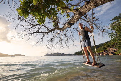 Beautiful sunny day on beach. happy man on swing enjoying holiday in seychelles.