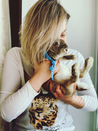 Young woman holding rabbit against face sitting at home