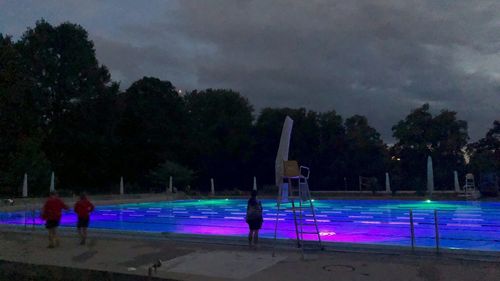 People by swimming pool at park against sky at night