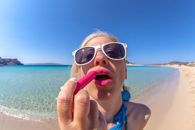 Woman applying lipstick at beach against sky