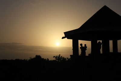Silhouette people standing at gazebo against sky during sunset