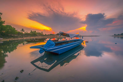 Boat moored in lake against sky during sunset