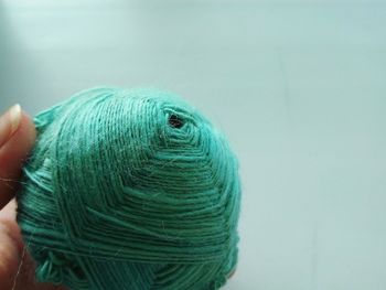 Close-up of hand holding green wool ball against colored background