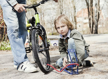 Portrait of boy filling bicycle tire with foot pump while father standing on road