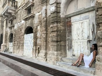 Full length of woman sitting by abandoned door