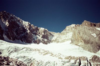 Low angle view of snowcapped mountains against clear blue sky