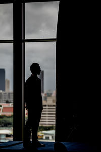 Rear view of silhouette man looking through window