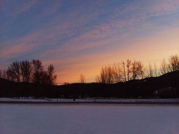 Snow covered field against sky during sunset