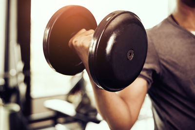 Midsection of man lifting dumbbell at gym