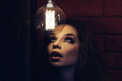 Young woman looking at illuminated light bulb in darkroom