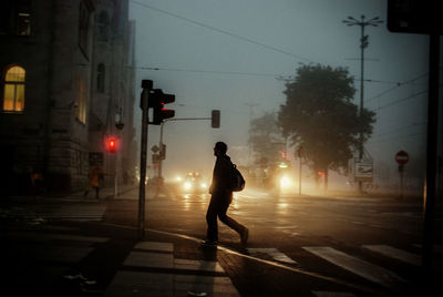 Full length of man crossing city street at dusk during foggy weather