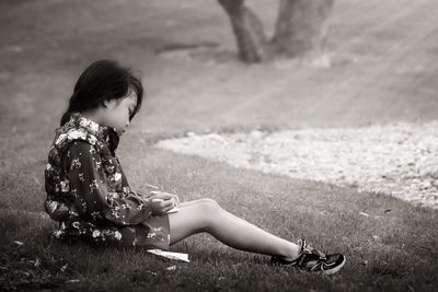 Side view full length of girl sitting on grassy field