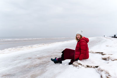 A woman in warm winter clothes rests sitting on the beach