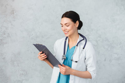 Young woman using phone while standing on wall
