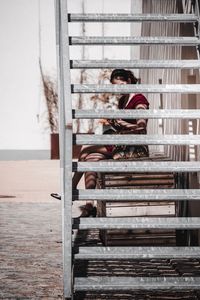 Side view of woman sitting behind staircase