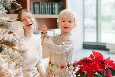 Happy caucasian mother with baby girl decorating christmas tree with ornaments baubles toys. happy f