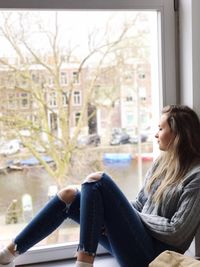 Thoughtful woman sitting on window sill at city