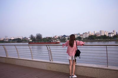 Full length rear view of woman standing on railing against sky