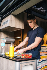 Young male traveler preparing healthy breakfast with natural juice and fresh berries inside camper van during summer holidays