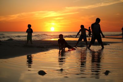 Silhouette children playing on beach against sky during sunset