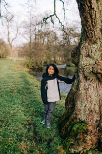 Portrait of young woman standing on tree trunk