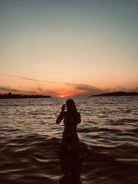 Silhouette man standing in sea against sky during sunset