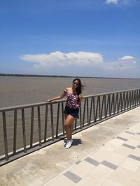 Full length of woman standing by railing against sea