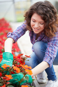Smiling young woman picking flowers in greenhouse