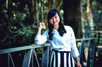 Portrait of young woman standing against trees