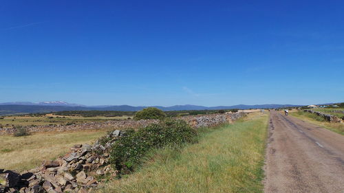 Road passing through field against clear blue sky