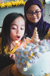 Close-up of girl blowing birthday candles with sister in party