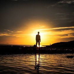 Silhouette people standing on beach at sunset