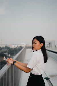 Young woman standing by railing against sky