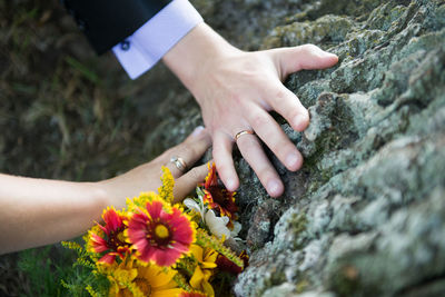Cropped image of bride and groom hands touching rock