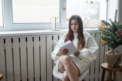 Merry christmas and happy new year. woman in warm white winter sweater sitting next to the window 