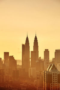 Modern buildings and petronas towers in city against sky during sunset