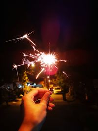 Cropped hand holding sparkler against illuminated city at night