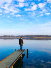Man standing on pier by lake against sky
