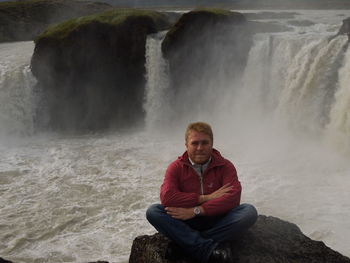 Man sitting on rock against waterfall