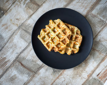 Vegetable waffles from zucchini and herbs on a dark plate close-up top view