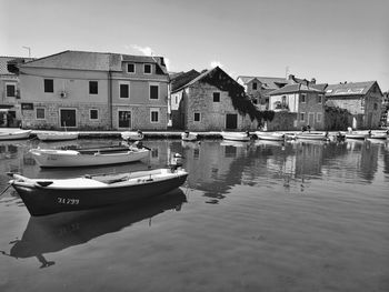 Boats moored on canal by buildings in city against sky