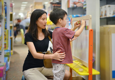 Boy by mother playing with toy at shopping mall