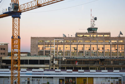 Construction site by buildings against sky during sunset