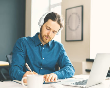 Male office worker dressed in casual clothes in headphones watching online webinar on laptop