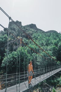 Rear view of shirtless man on footbridge against sky